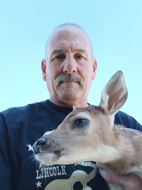 Man holding a deer fawn outdoors against a blue sky