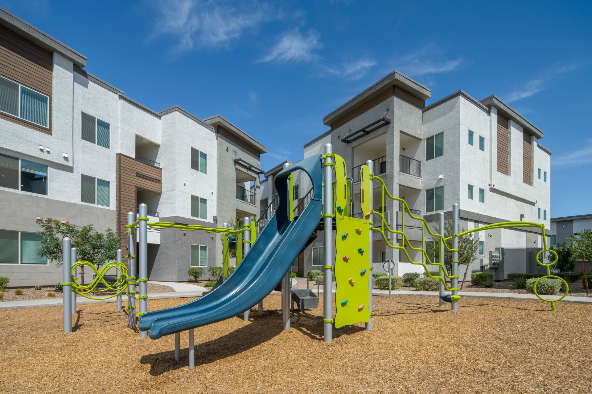 Playground with slide and climbing wall in front of apartment buildings at Lumina Mountain Vista in Mesa, AZ.