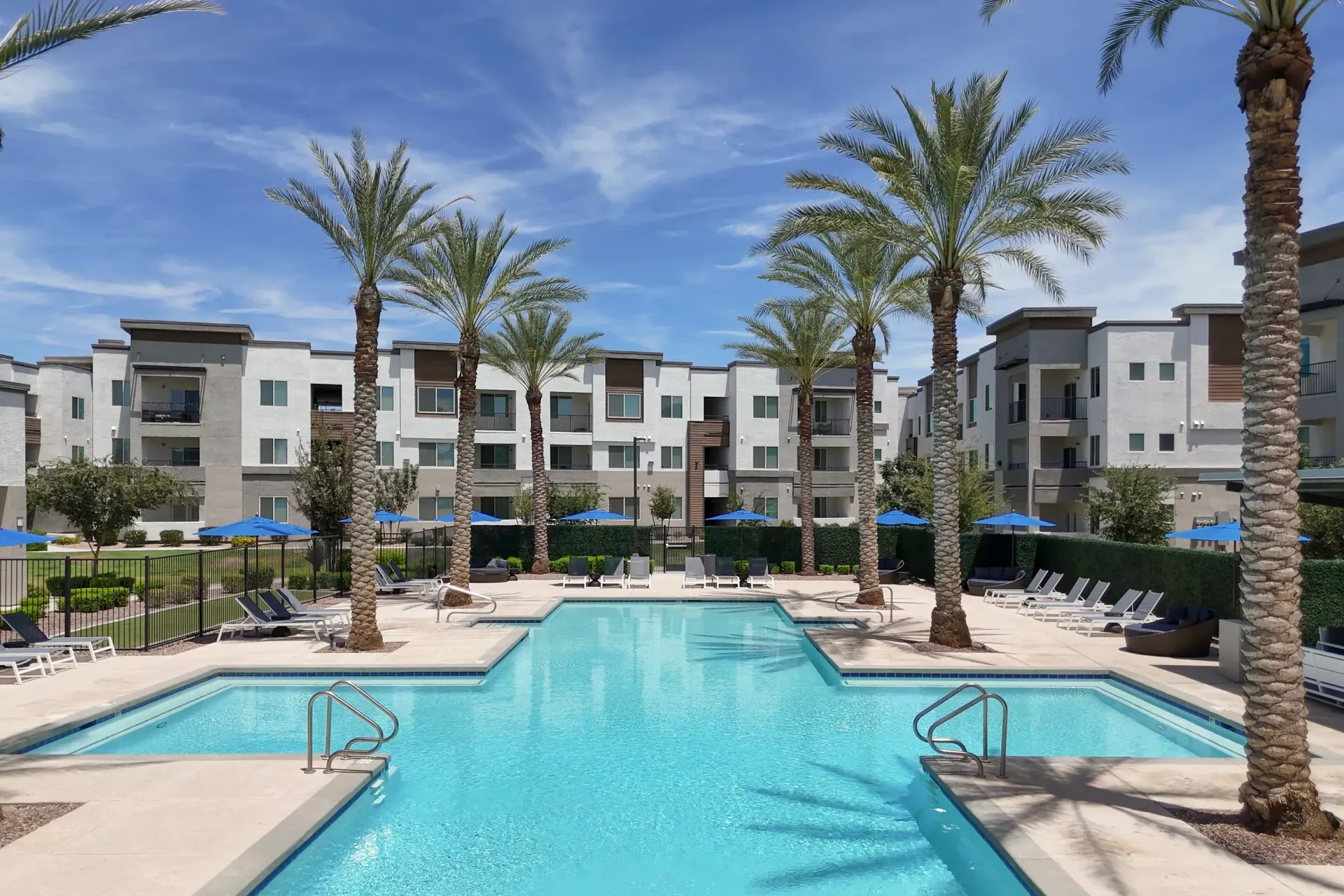 Outdoor swimming pool with lounge chairs and palm trees in front of apartment buildings at Lumina Mountain Vista in Mesa, AZ.