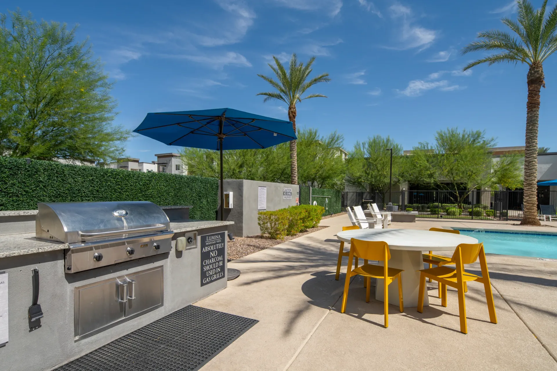 Outdoor grilling station with stainless steel grill, adjacent to a swimming pool and seating area at Lumina Mountain Vista in Mesa, AZ.
