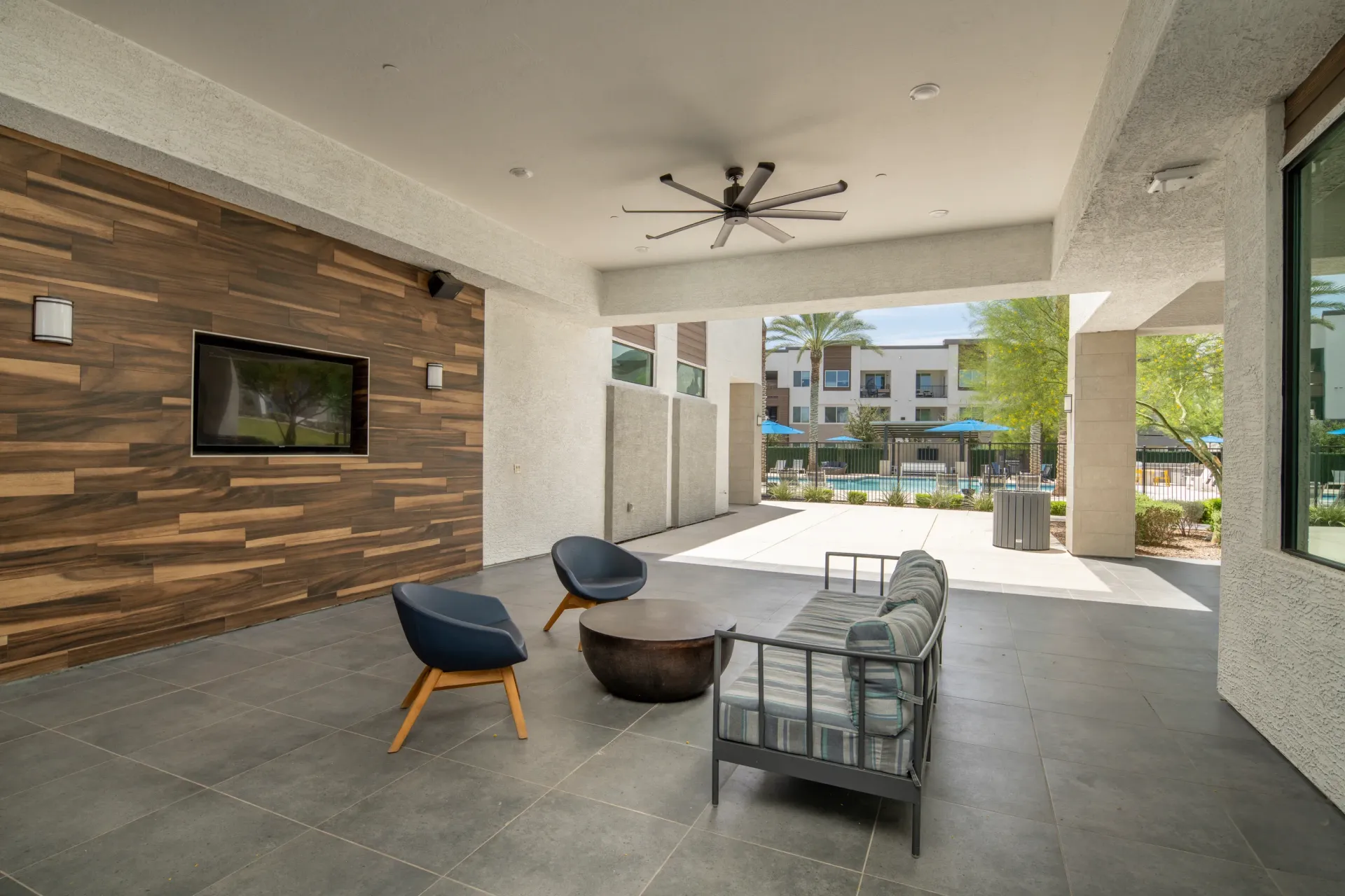 Outdoor lounge area with seating and a TV, overlooking the pool at Lumina Mountain Vista in Mesa, AZ.