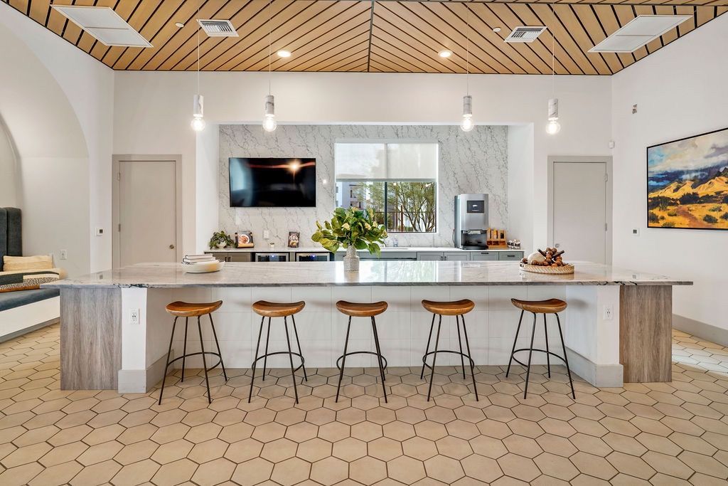 Modern communal kitchen with marble island and six wooden bar stools.