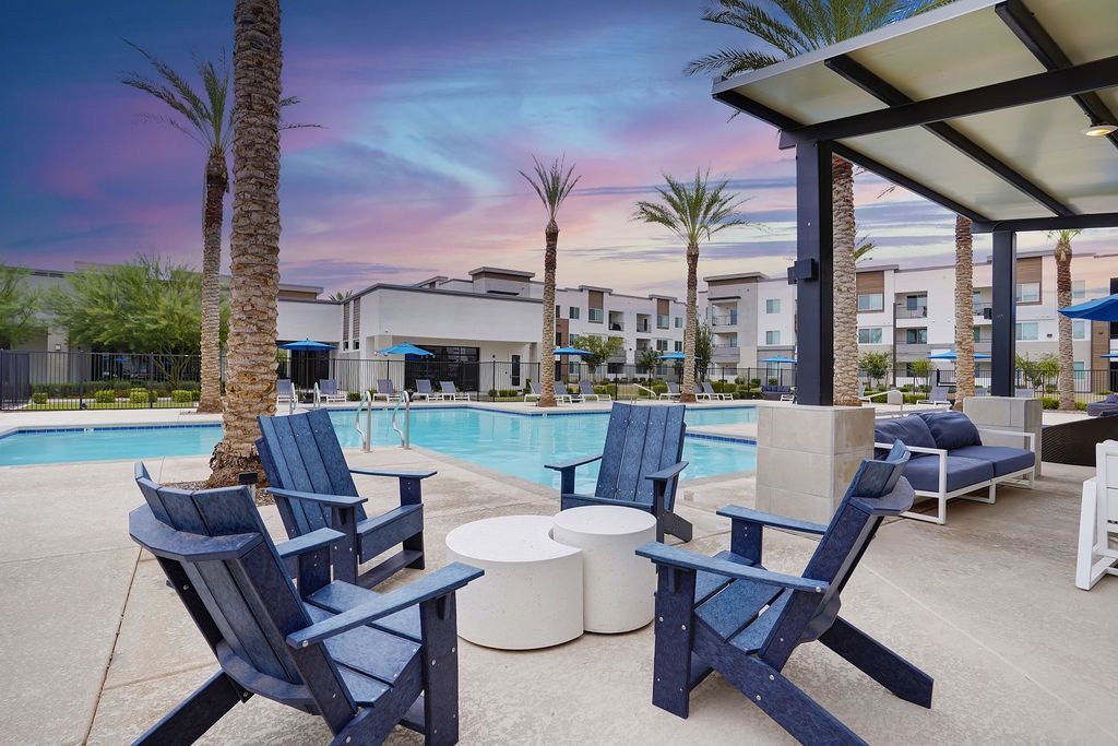 Outdoor pool area at an apartment complex with palm trees and blue lounge chairs.