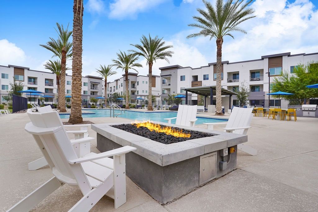Outdoor community pool area with a fire pit, lounge chairs, and palm trees.