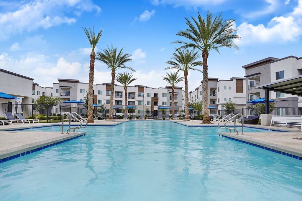 Outdoor communal pool area with palm trees, lounge chairs, and apartment buildings in the background.