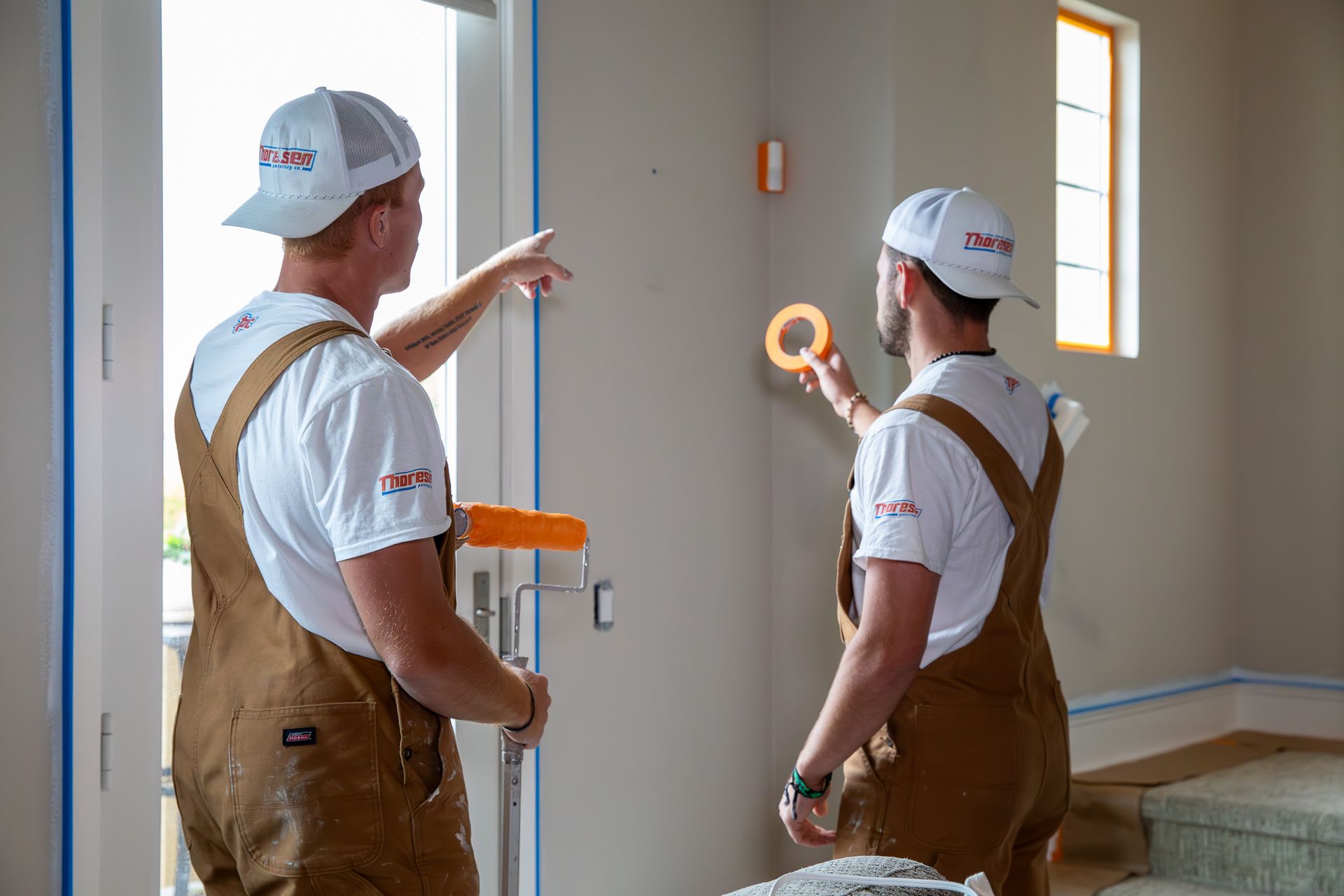 Two painters from Thoresen Painting Co. are prepping to paint a room inside a house.