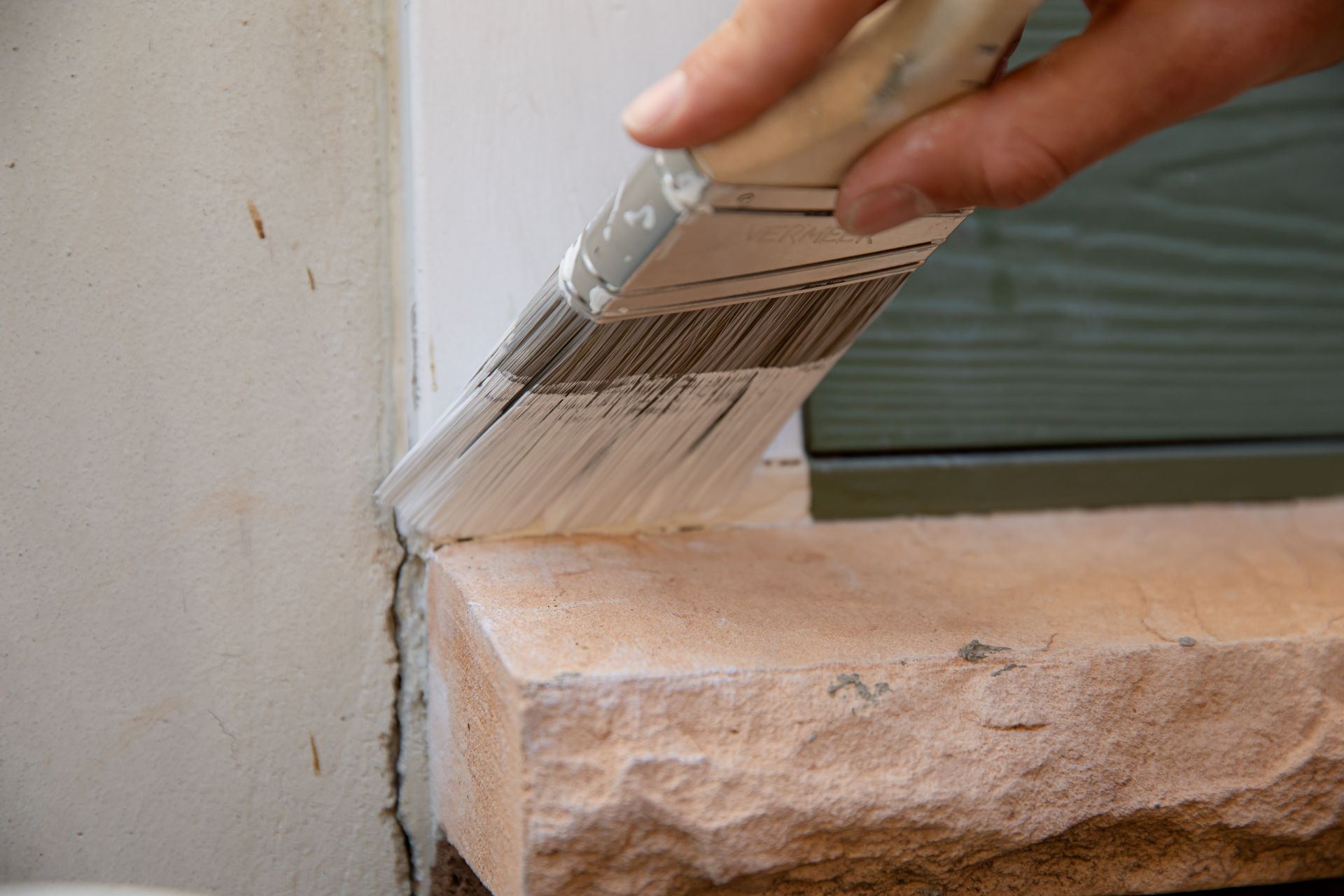 A person is painting a window sill with a brush.