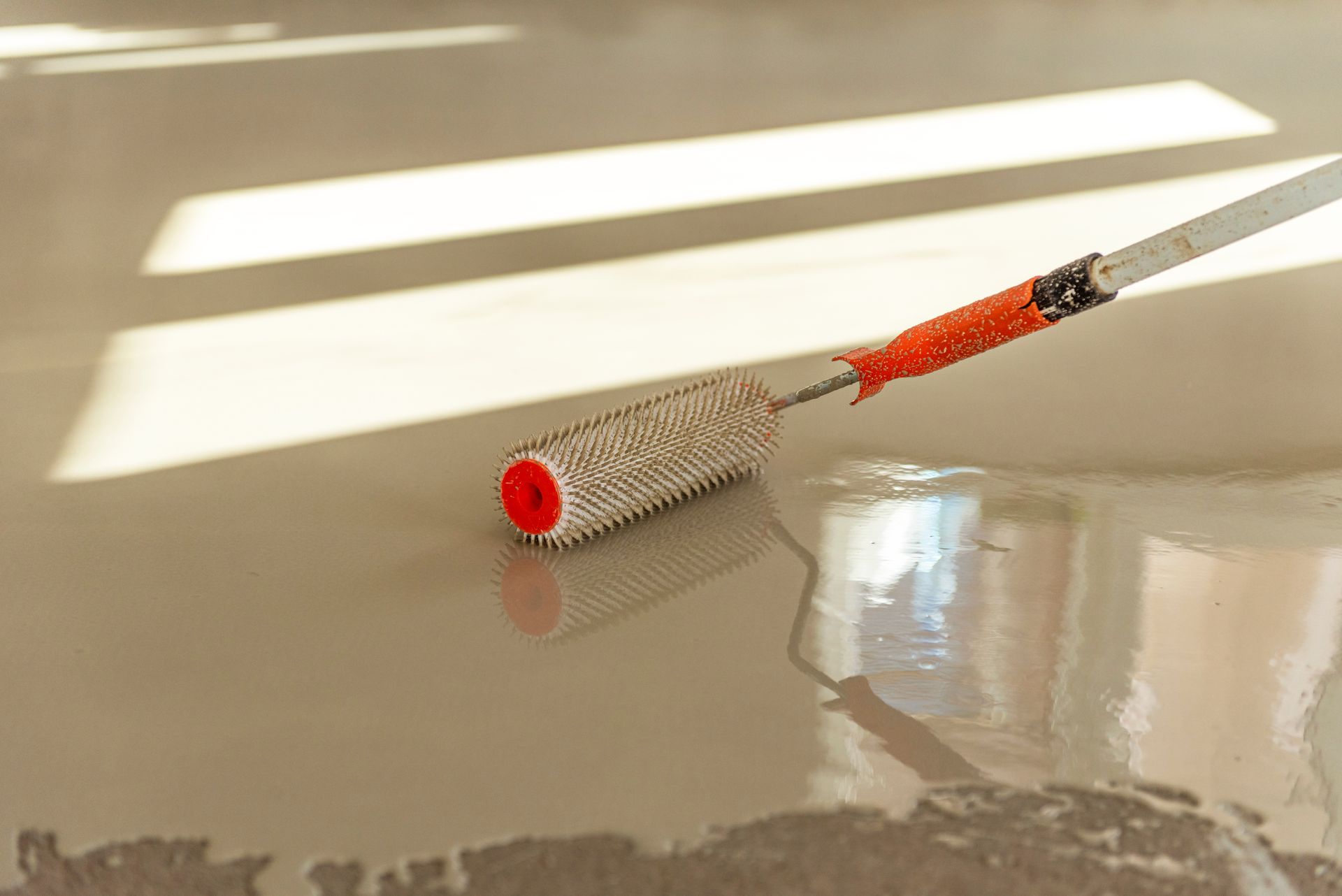 A roller is being used to install epoxy flooring in a room.