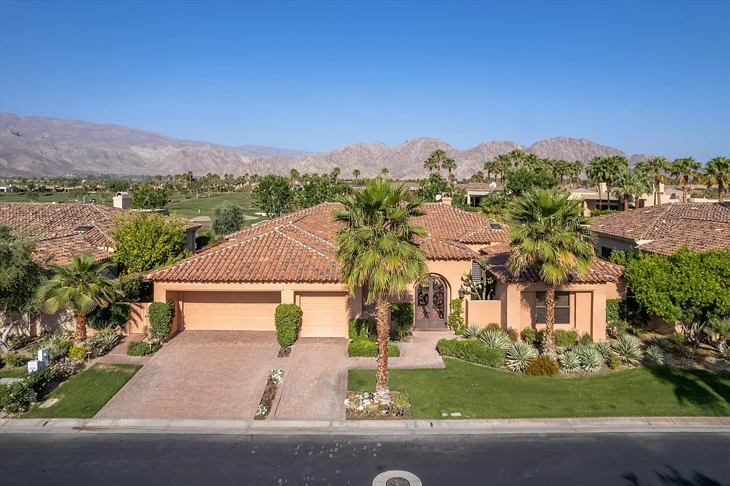 An aerial view of a house with palm trees and mountains in the background.