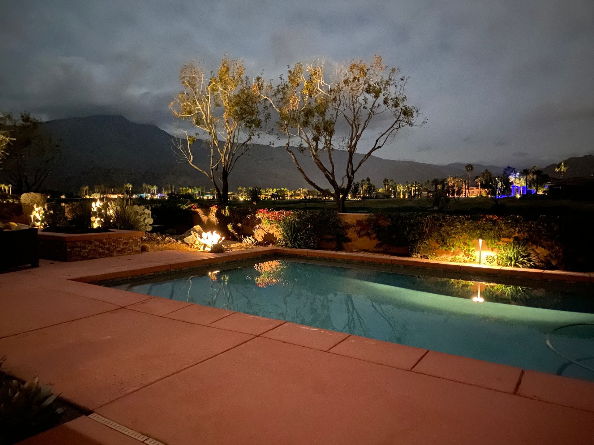 A swimming pool is lit up at night with mountains in the background
