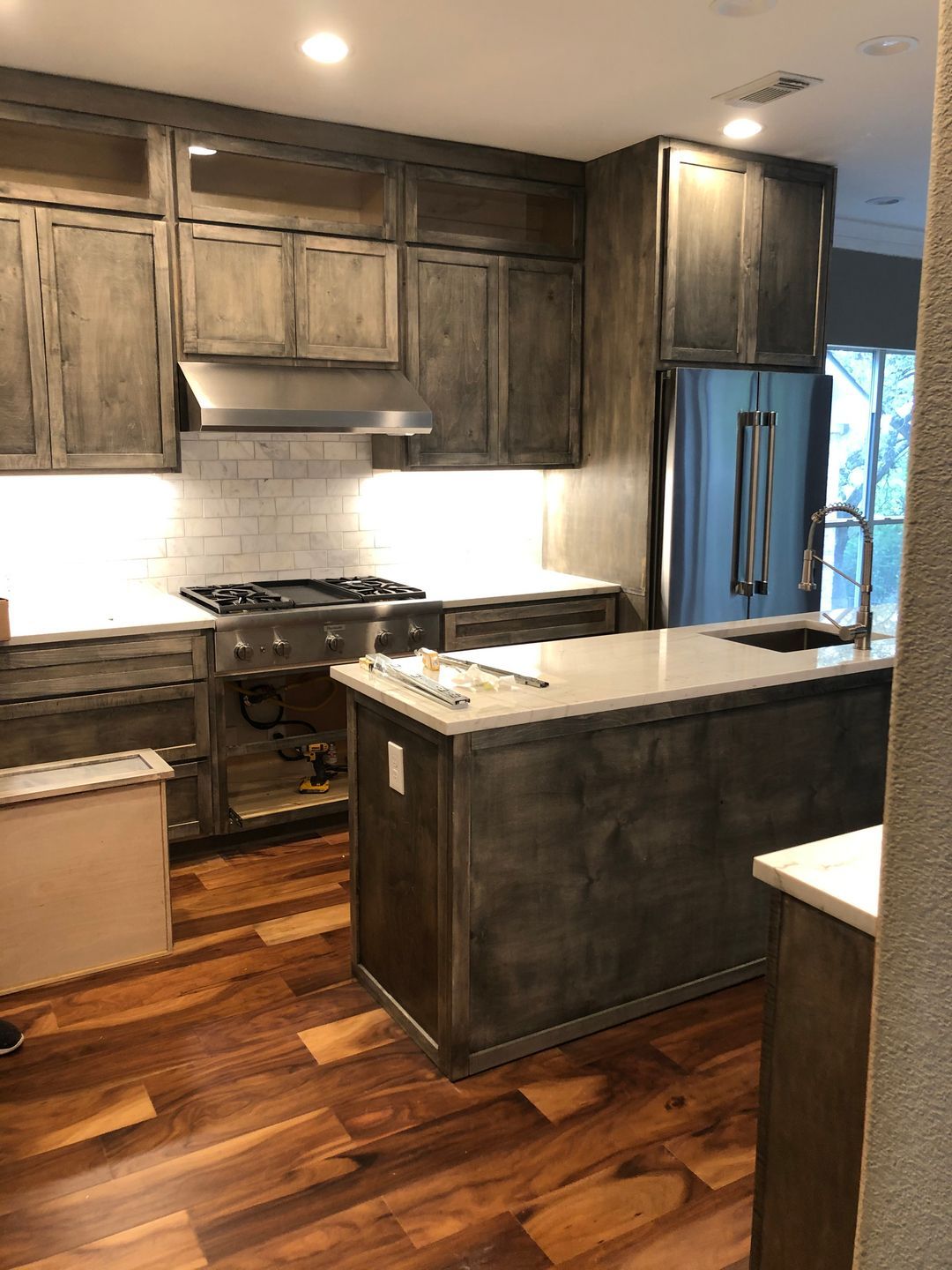 A kitchen with wooden floors , stainless steel appliances , and a large island.