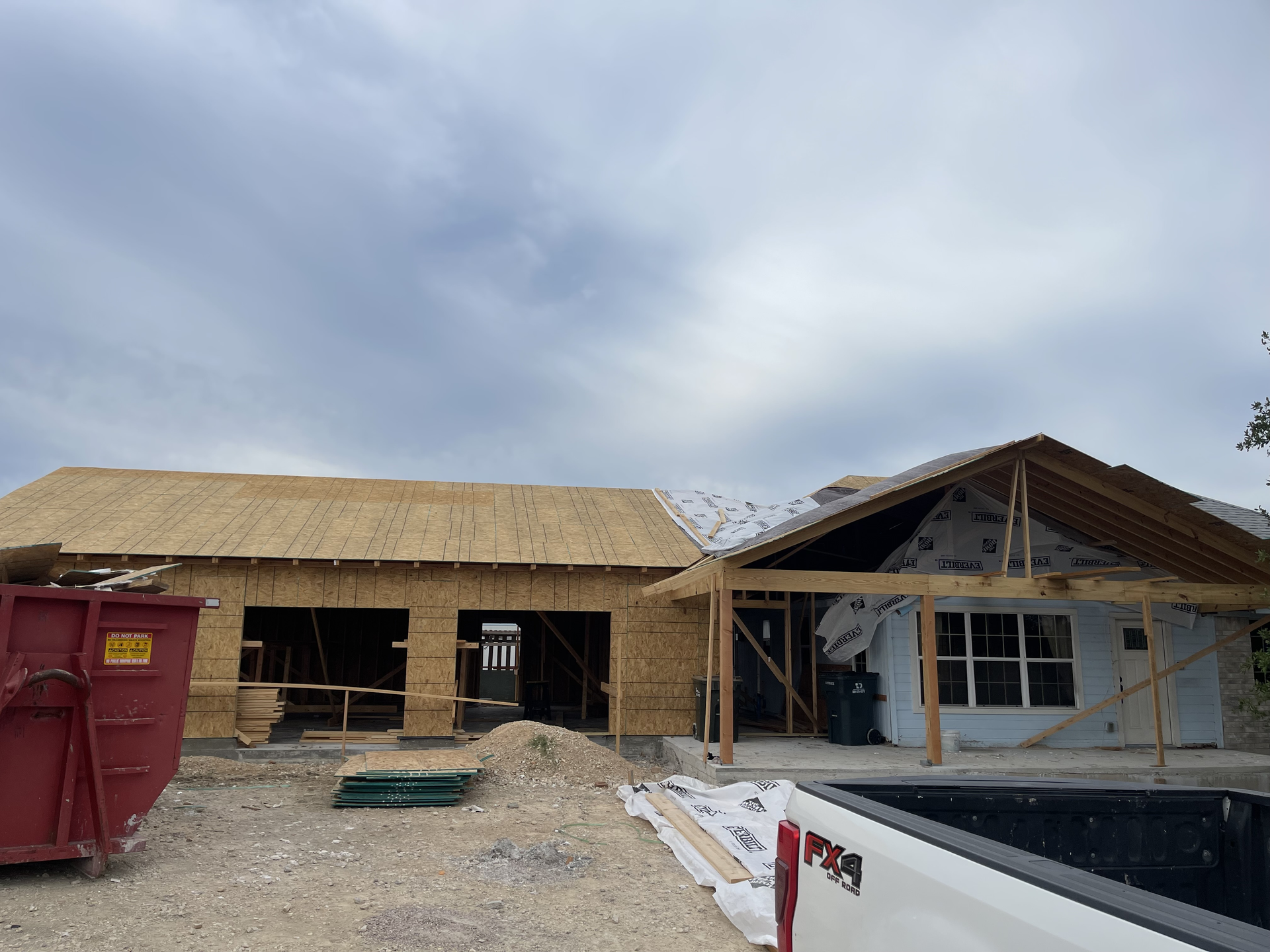 A house is being built with a red dumpster in front of it.