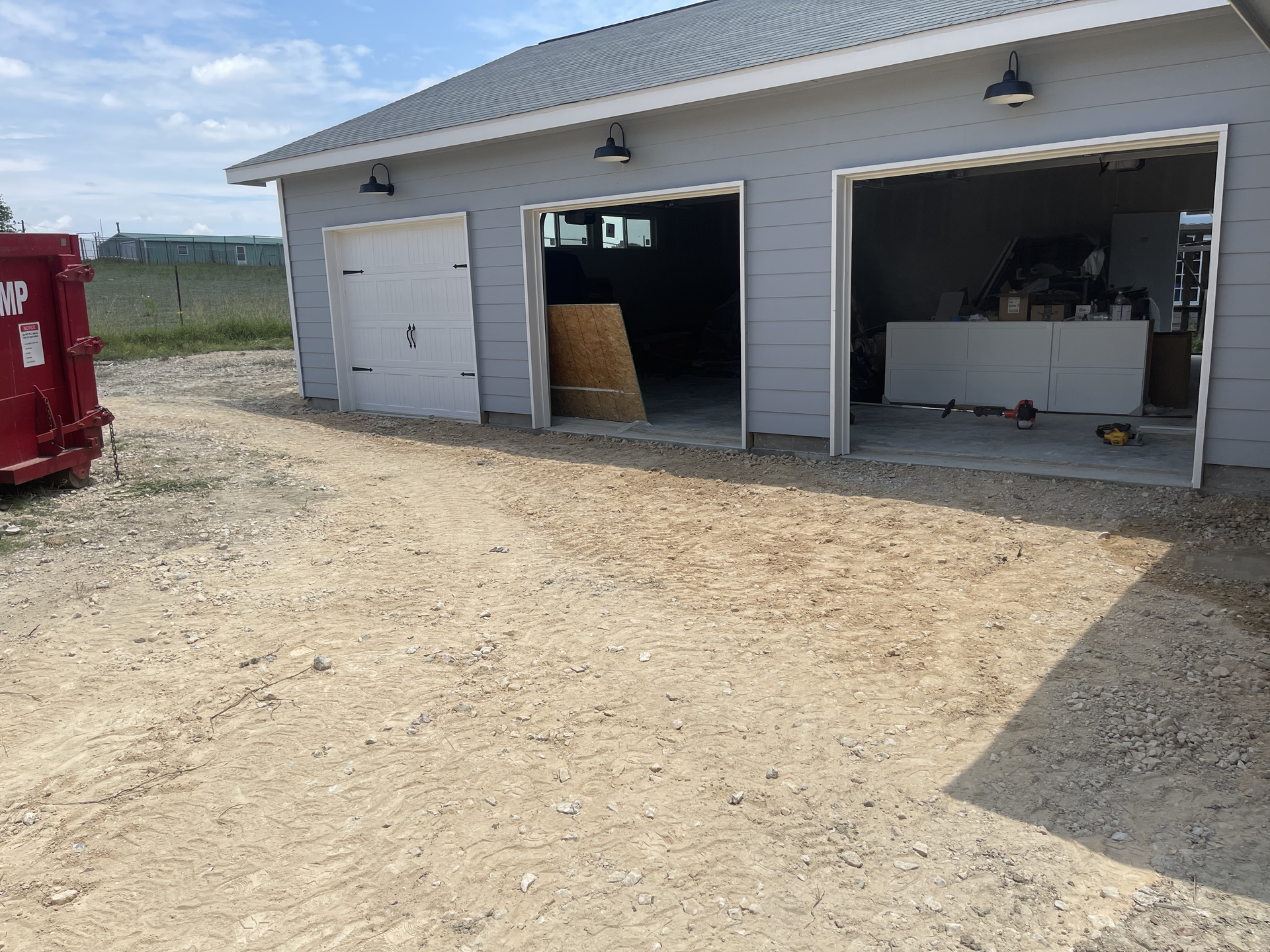 A garage with the doors open and a dumpster in front of it.