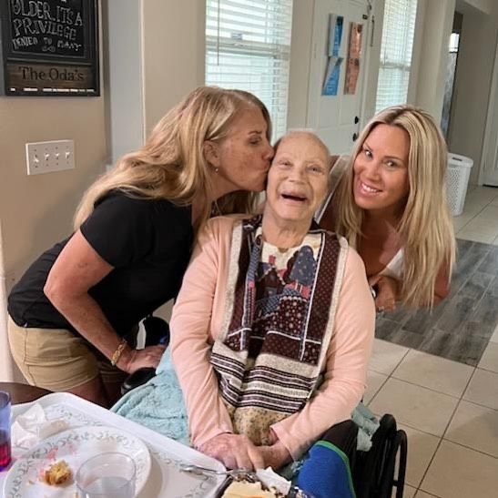 Two women are kissing an elderly woman in a wheelchair.