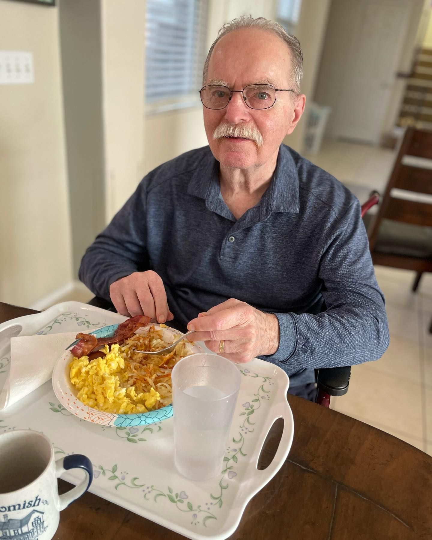 A man in a wheelchair is sitting at a table eating breakfast.