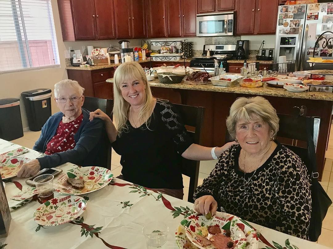 Three women are sitting at a table in a kitchen eating food.