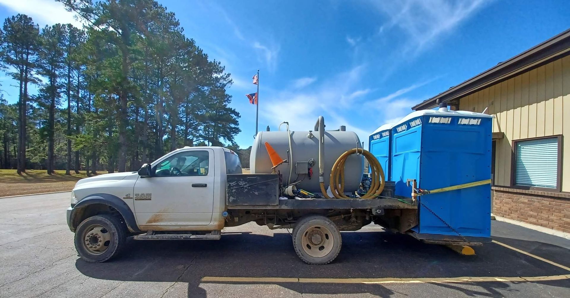 White utility truck with tank and blue equipment parked beside a beige industrial building under a clear sky