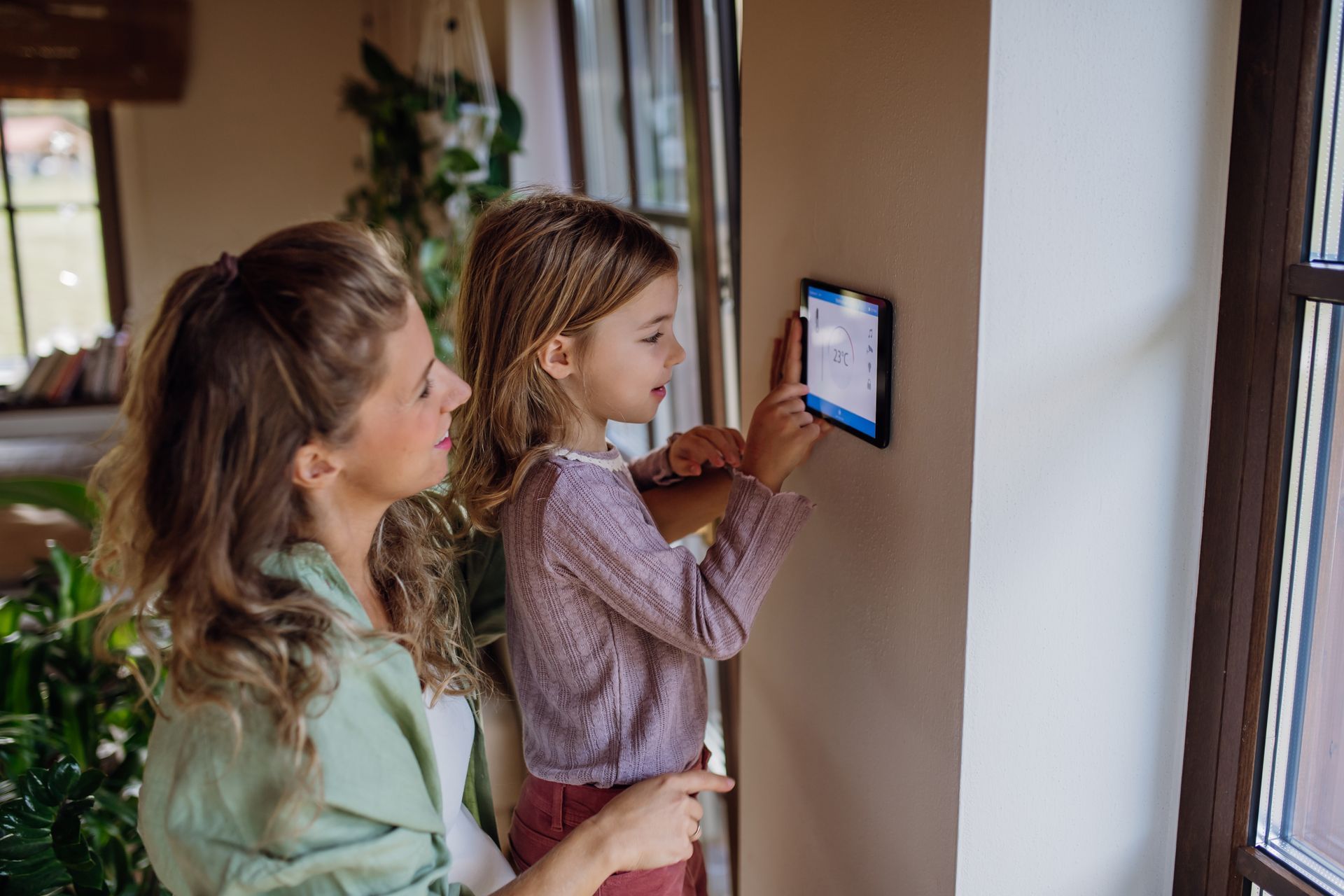 Two people using a wall-mounted tablet in a bright home hallway