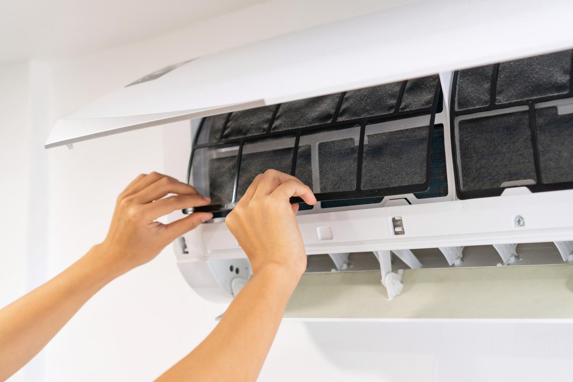 Hands cleaning a wall-mounted air conditioner filter unit