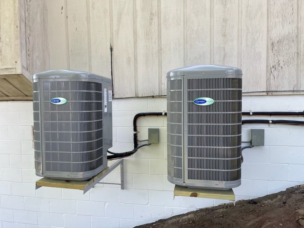 Outdoor air conditioner unit beside a house with blue shutters and green shrubs
