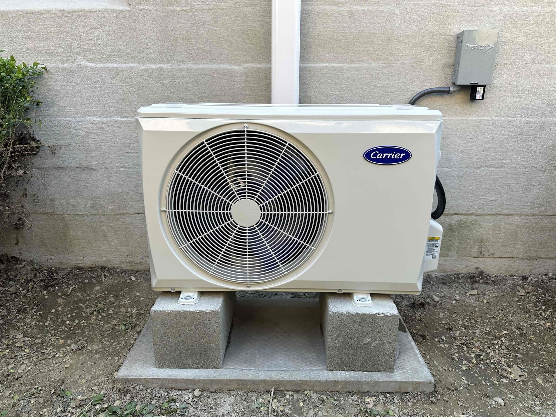 A carrier air conditioner is sitting on top of concrete blocks next to a wall.