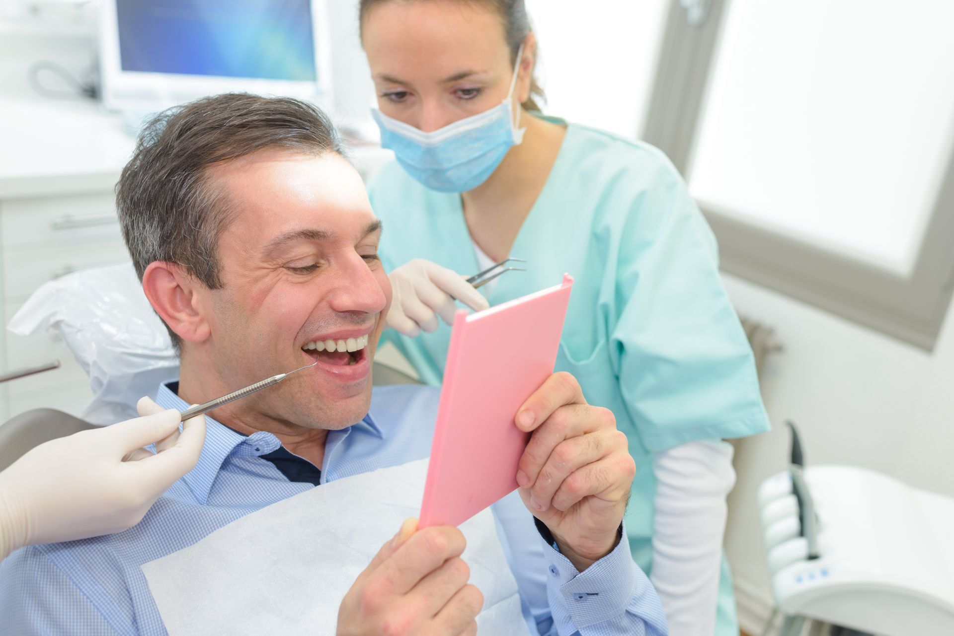 A man is sitting in a dental chair looking at his teeth in a mirror.