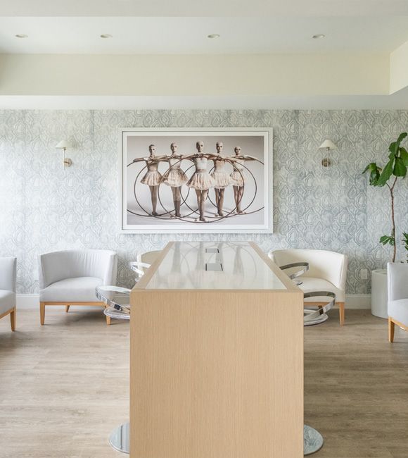 Bright modern living room with white chairs, wood table, patterned wall art, and light wood flooring
