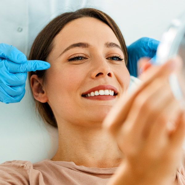 Woman smiling while receiving an ear treatment with blue-gloved hands