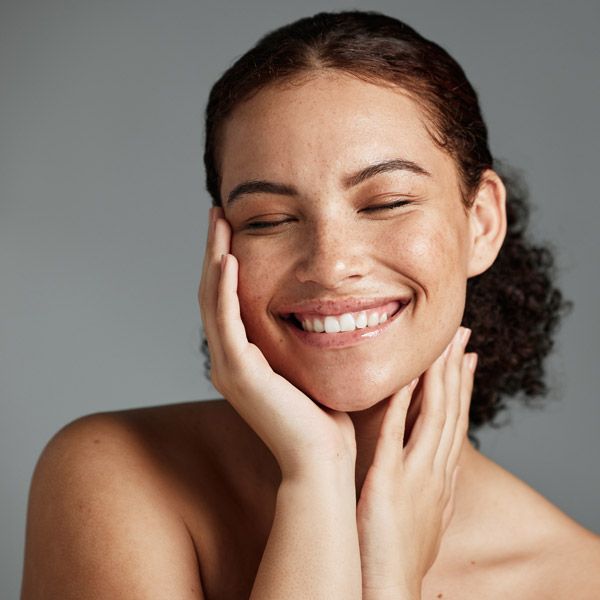 Smiling person with eyes closed, resting face on hands 