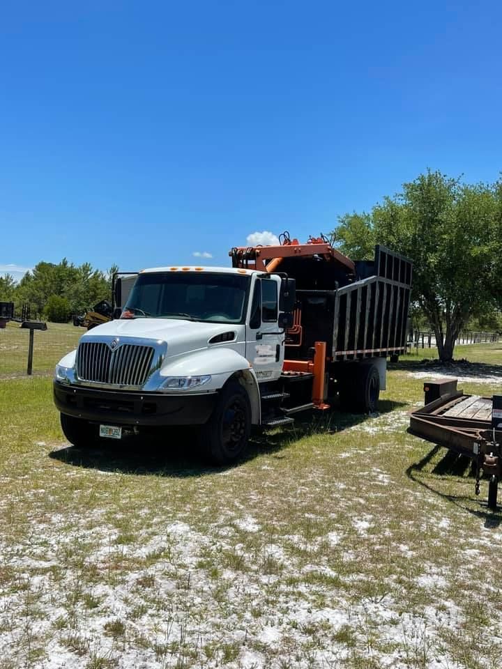 A white truck with a crane on the back is parked in a grassy field.