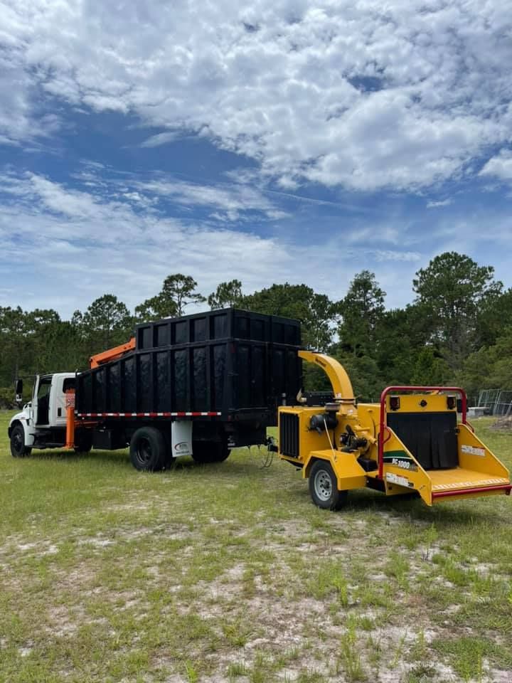 A dump truck with a chipper attached to it is parked in a grassy field.