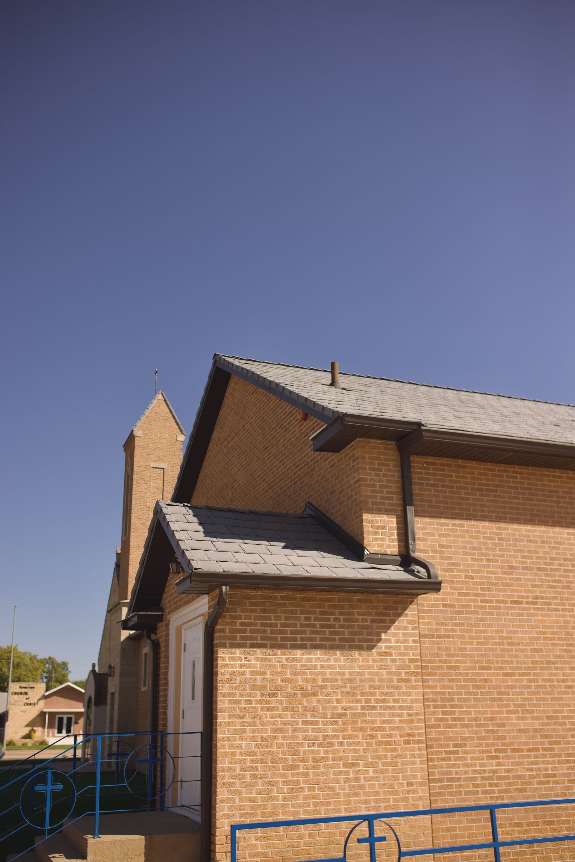 Brick church building with a gray roof and blue metal fence under a clear blue sky