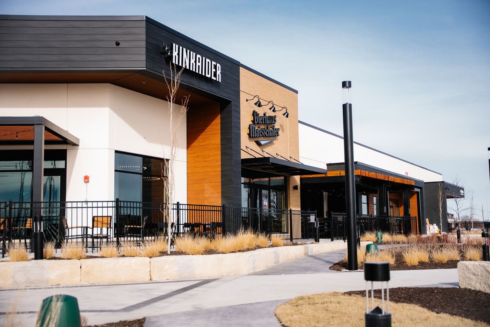 Modern restaurant building with a patio, large windows, and a sign near the entrance.