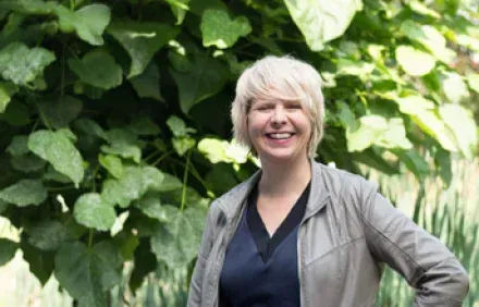 Een vrouw staat voor een boom en glimlacht.