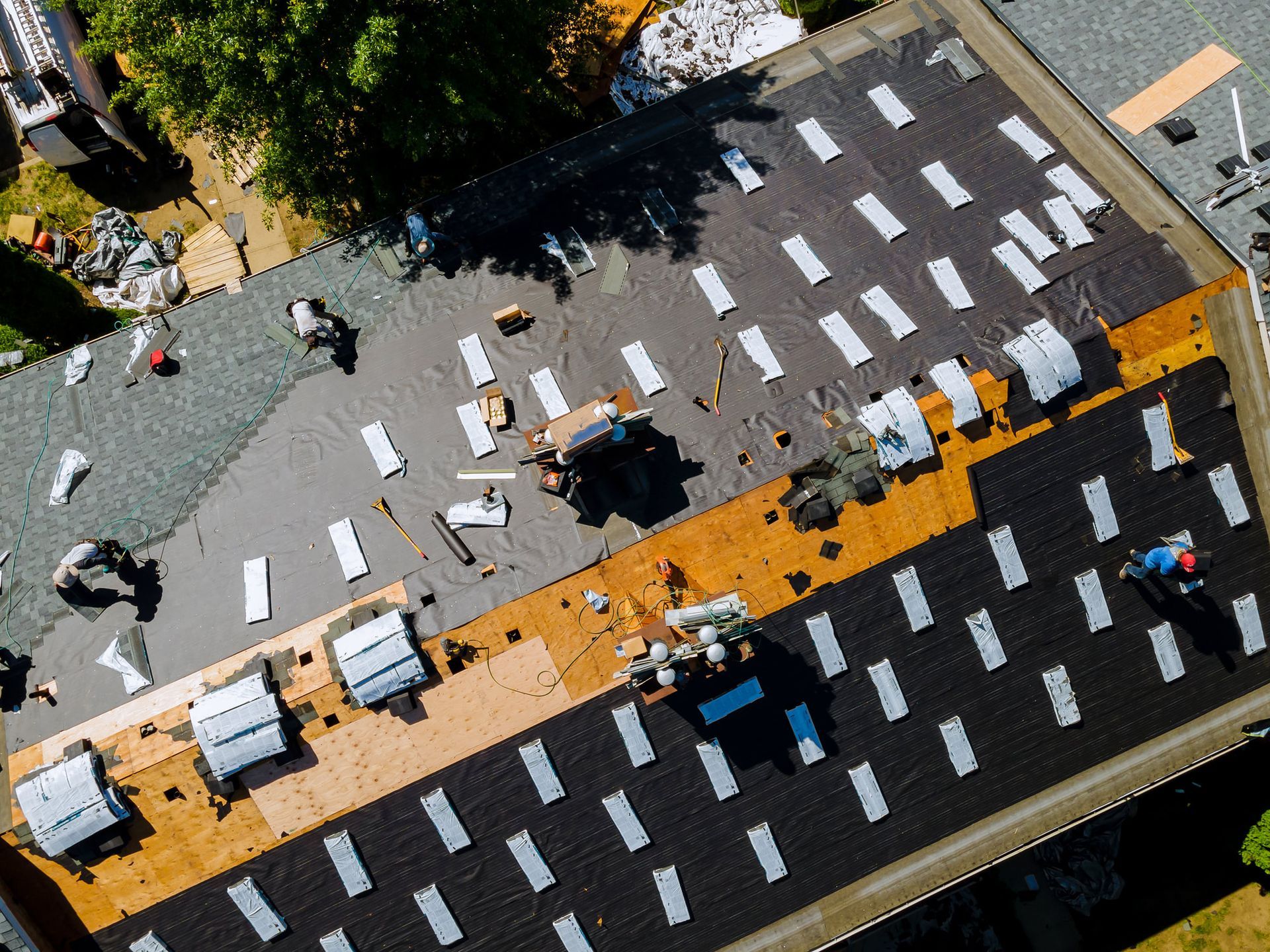 Roofers working on a building roof, removing old shingles and installing new ones; aerial view.