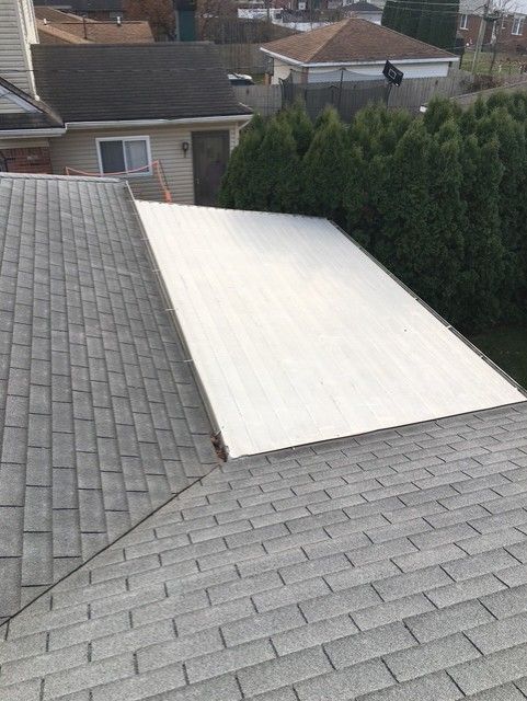 A commercial roof with grey shingles next to a flat, white-covered roof section.