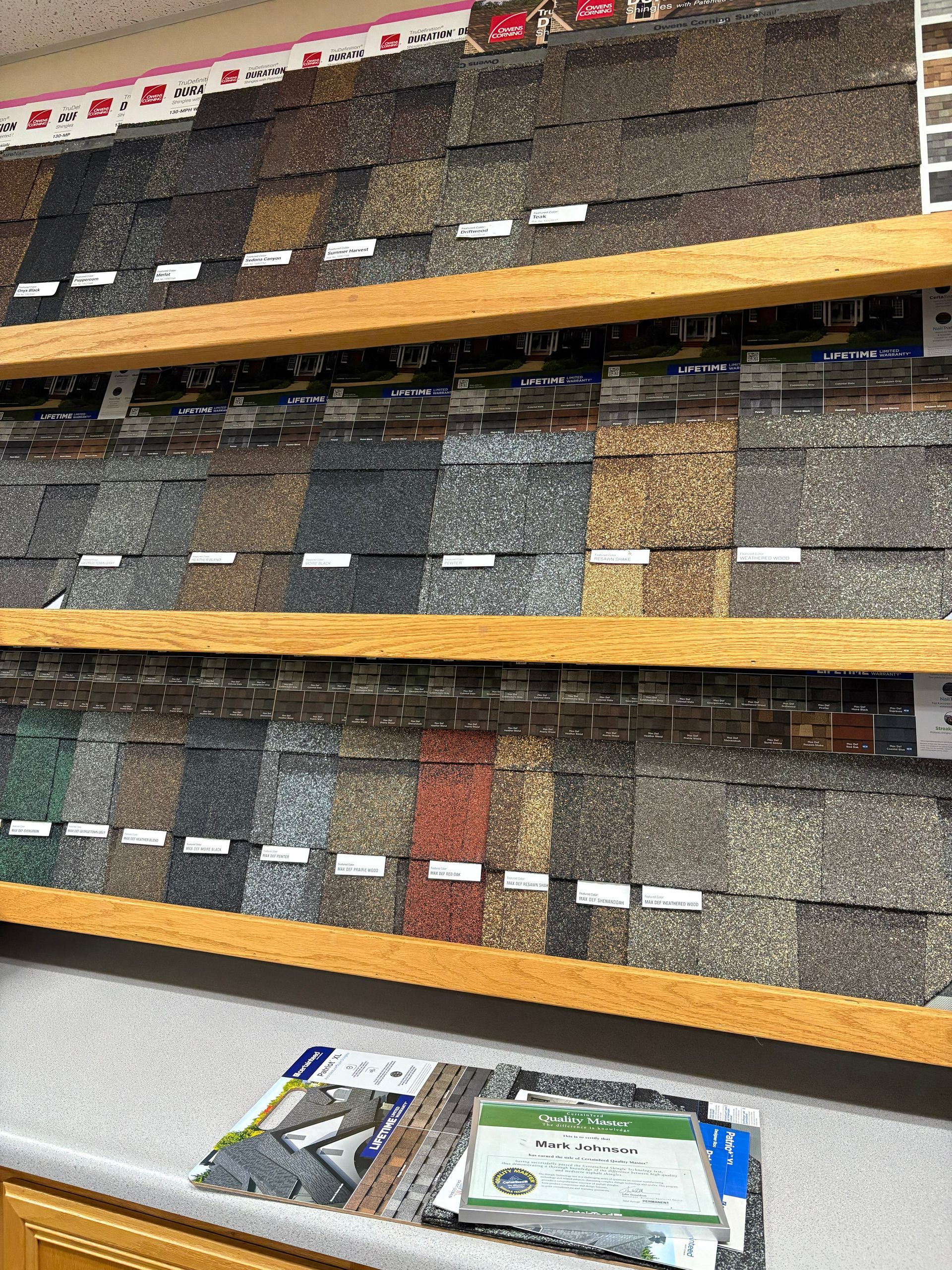 Display of roofing shingle samples in various colors and textures on wooden shelves.