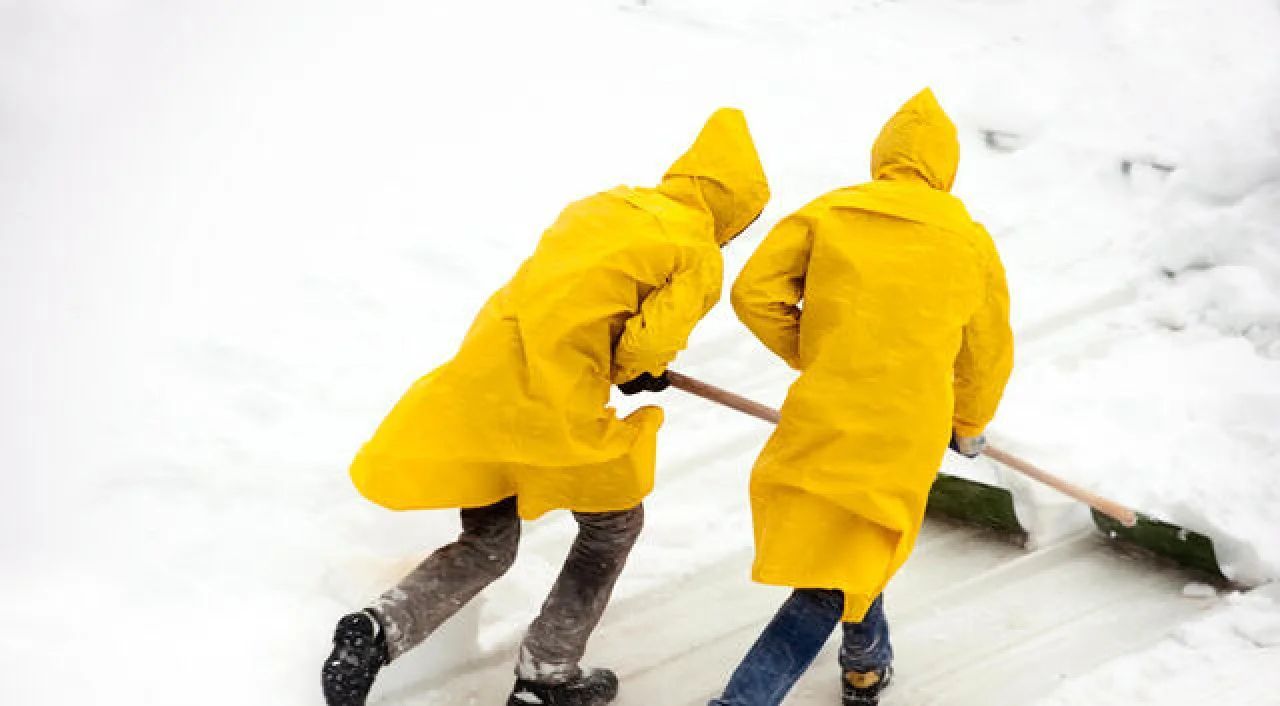 Two people in yellow raincoats shoveling snow together outdoors