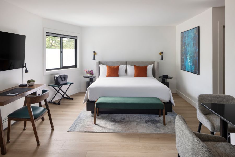 Modern studio apartment with kitchen, living area, and bed; wood floors, white walls, and turquoise accents.
