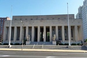 A stone building with columns and steps, flanked by flagpoles, under a clear blue sky.