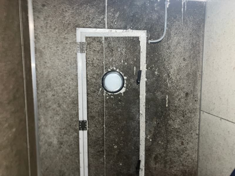 Door with a porthole, heavily stained and moldy, inside a dingy enclosure.