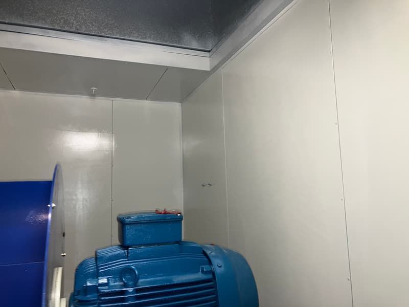 Interior view of a white-walled room with a blue motor and fan. A silver ceiling and vent are visible.