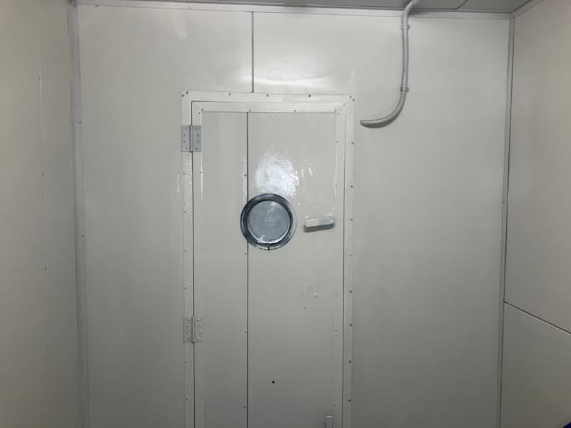 White interior room with a door with a porthole, and a metal handle.