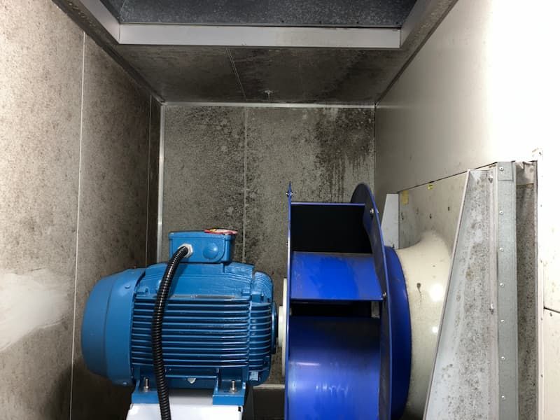 Blue electric motor and fan in a gray, enclosed space; walls appear dirty.