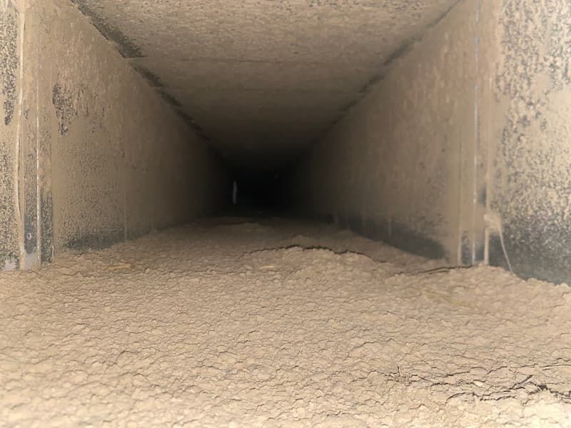 Inside of a dusty HVAC duct, coated with thick layer of debris.