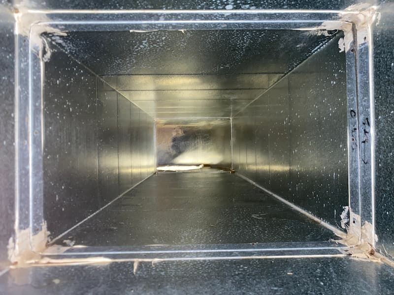 Inside view of a rectangular air duct, looking down a narrow passageway, with sealant at the edges.