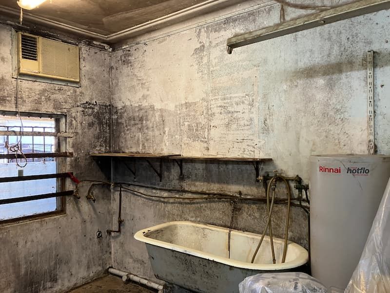 Moldy, abandoned interior with a bathtub, shelves, and water heater.