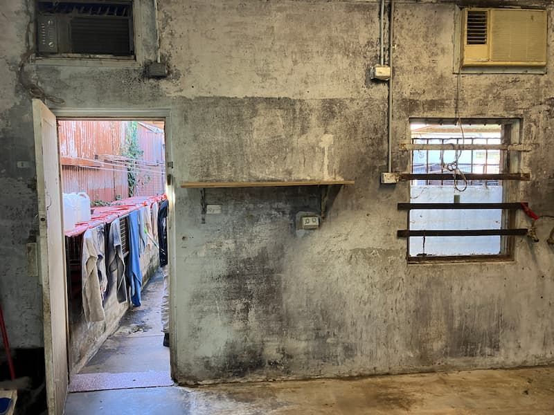 Concrete room with open doorway to laundry area, window with bars, shelf, and air conditioner.