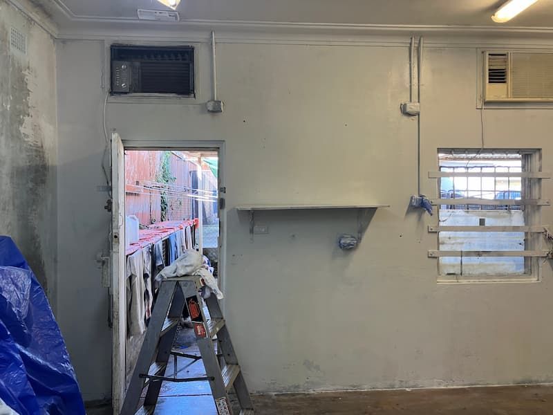Interior view of a room with painted walls, doorway, window, and air conditioning units. A ladder sits near the open doorway.