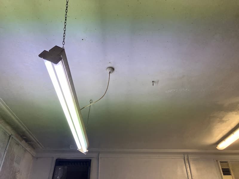 Fluorescent light fixture hanging from a stained ceiling.
